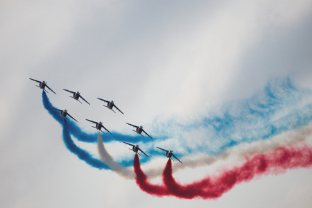 Several military aircraft symmetrically perform aerobatics figures releasing a multicolored smokeの写真素材