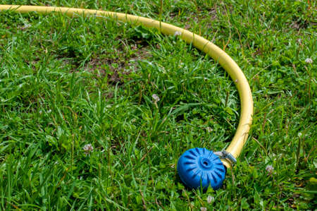 Yellow hose with sprinkler for watering plants. Drought and water conservation. Turned out without water on the grassの写真素材