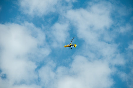 A yellow motorized hang glider with a propeller soars in the blue sky against the background of cloudsの写真素材