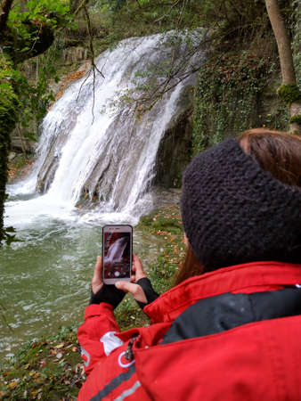 Girl taking a picture of a waterfall in nature. Hiking and environment.
