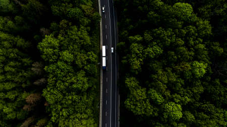 Long road going through the green forest, who has not end. On this road we can see some cars and trucks. Photo from above.の写真素材