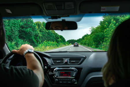 Hands of a driver on steering wheel of a car and empty asphalt road. Forest on the sides