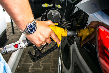 Pumping gas at gas pump. Closeup of man pumping gasoline fuel in car at gas station. Watch on the handの写真素材