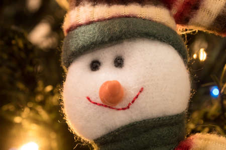Smiling snowman on Christmas Tree with Green wool cap and scarf. Christmas lights at background.