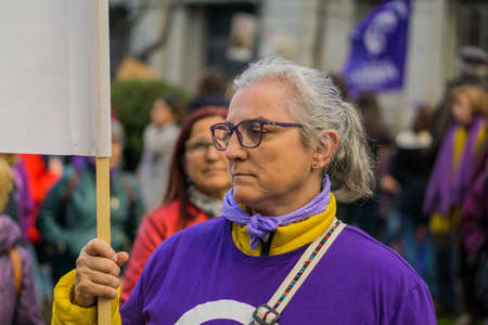 An old Woman with black glasses holding a protest sign during 8M marches in the International...