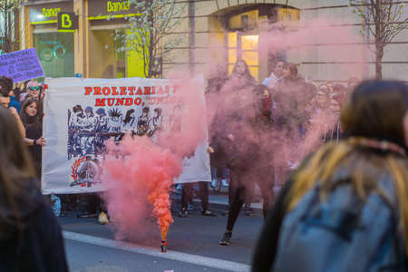 A Crowd marching with signs in middle of orange smoke flare during 8M marches in the International Women's Day by claiming her rightsのeditorial素材