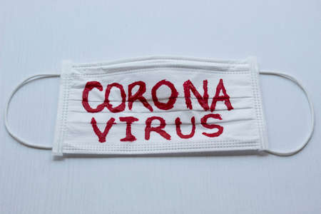 Closed up to white face mask with red CORONAVIRUS inscription and with white blackground. COVID-2019