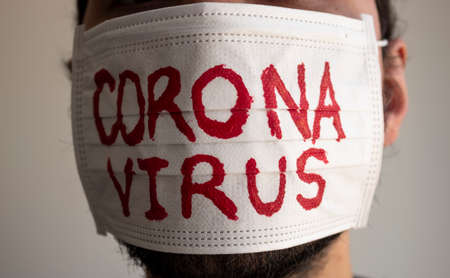 Closed up to a CORONAVIRUS man patient with beard using a white face mask with red CORONAVIRUS inscription. Concept photography COVID-2019の写真素材