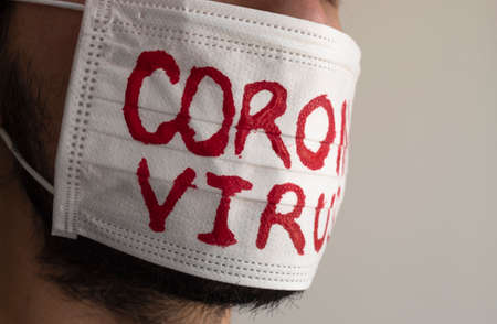 Closed up to a CORONAVIRUS man patient with beard using a white face mask with red CORONAVIRUS inscription. Concept photography COVID-2019の写真素材