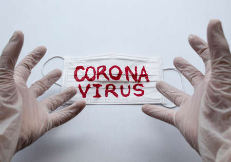 Closed up to White Sterilized gloves making a surprised hand expression over yellow face mask with Black CORONAVIRUS inscription with white blackground. COVID-2019の写真素材