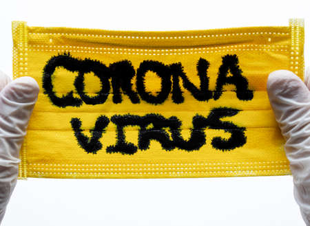 Closed up to Yellow Face Mask with CORONAVIRUS inscription and two hands with White Gloves or Esterilized globes holding them. COVID-2019の写真素材