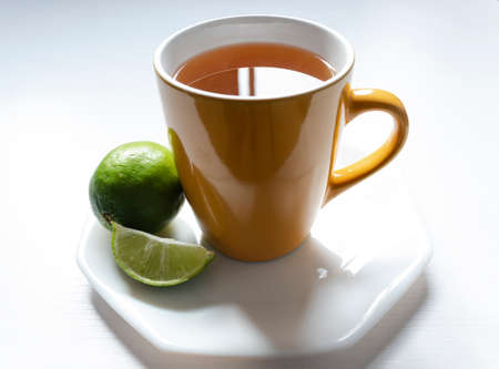 A yellow mug with Colombian traditional hot drink knowed as AGUA DE PANELA with lemon and white background. This hot drink is useful to a illness and its used to a meal too.の写真素材