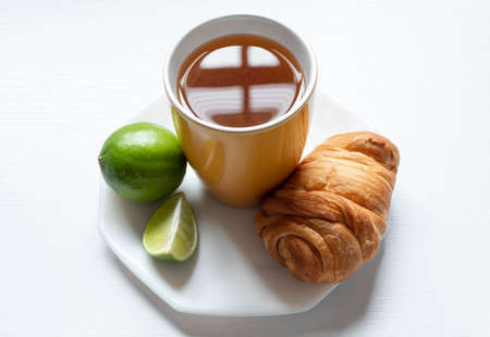 A top view of a yellow cup with Colombian traditional hot drink knowed as AGUA DE PANELA with lemon, one bread and white background. This hot drink is useful to a illness and its used to a meal too.の写真素材