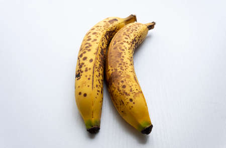 Close up to a two yellow freckled bananas in vertical form over a white wooden table.の写真素材