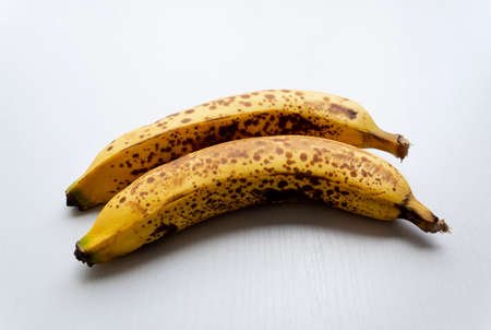 Close up to a two yellow freckled bananas in over a white wooden table.の写真素材