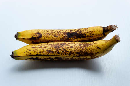 Close up to a two yellow freckled bananas in horizontal form over a white wooden table.の写真素材