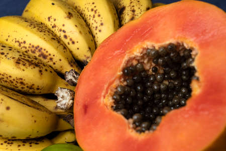Close up to a fresh sliced orange papaya with seeds inside, freckled bananas cluster and lemons at background. Fruit and eating concept photographyの写真素材