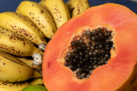 Close up to a fresh sliced orange papaya with seeds inside, freckled bananas cluster and lemons at background. Fruit and eating concept photographyの写真素材
