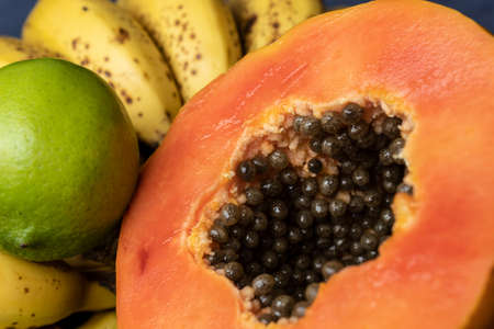 Close up to a fresh sliced orange papaya with seeds inside, freckled bananas cluster and lemons at background. Fruit and eating concept photographyの写真素材