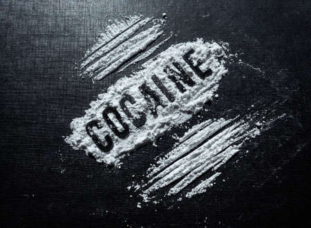Closeup to Cocaine black lettering in middle of white cocaine with lines over black background. Drugs and Addiction conceptの写真素材