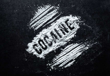 Closeup to Cocaine black lettering in middle of white cocaine with lines over black background. Drugs and Addiction conceptの写真素材