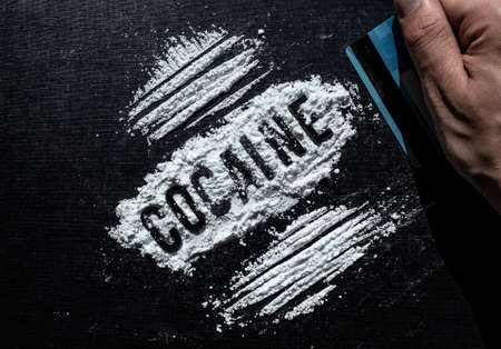 Closeup to a male hand hand holding a credit card making cocaine lines over a black background. Drugs conceptの写真素材