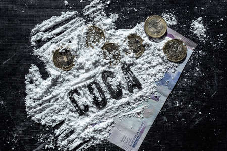 Closeup to a cocaine or COCA spanish lettering word over cocaine lines, colombian coins, colombian money paper and a blue credid card over a black background. Drugs and addiction conceptの写真素材