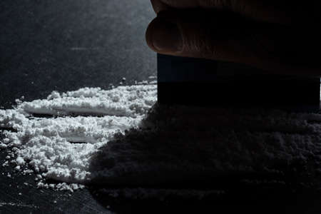 Closeup to a male hand hand holding a credit card making cocaine lines over a black background. Drugs conceptの写真素材
