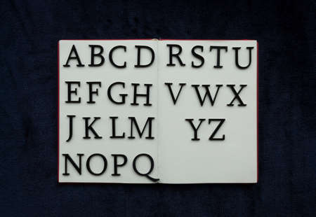 Close up to ALPHABET lettering over blank notebook at blue navy background. Reading and study concept photographyの写真素材