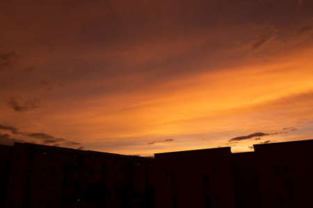 Stunning orange and yellow summer sunset with residential unit black silhouette and strange clouds formationsの写真素材