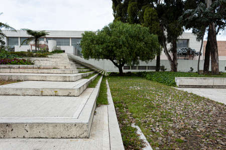 Geometric pattern of a modern white street stairways with green gardens, trees and big building at backgroundの写真素材