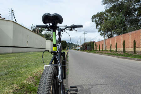 Closeup to a black mountain bike with reflective green signs at suburbs asphalt street near to a grass garden platform in sunny day with mountains at backgroundの写真素材