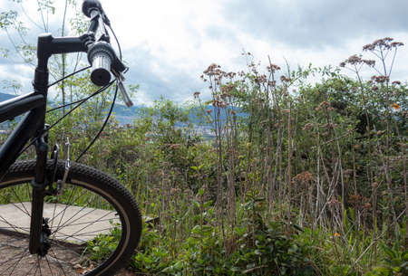 City landscape at the top of mountain view with green vegetation and black mountain bike front, handle bar and front tireの写真素材