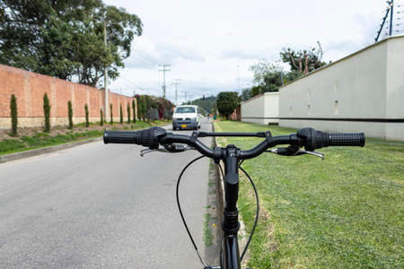 Close up to a black mountain bicycle handle bar with grips near to a green garden and blurred white van transit over asphalt way.の写真素材