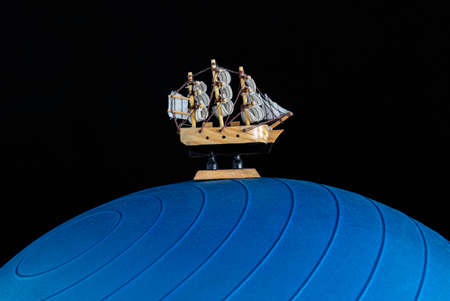 Small wooden boat over a blue giant fit ball and a black background. Travel and adventure concept photographyの写真素材