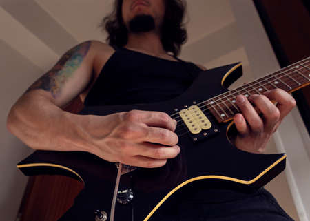 Bottom view of a young man playing a black and yellow electric guitar at indoor. Rock and music conceptの写真素材