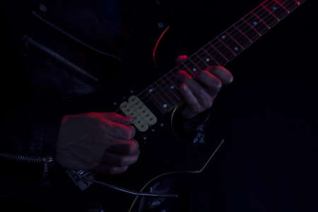 Long Exposure picture of a man wearing a leather jacket playing a black and yellow electric guitar at indoor illuminated with red and white lights. Rock and music conceptの写真素材