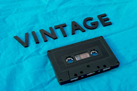 Top View of VINTAGE black lettering word with an old black cassette over a blue cloth. Fashion and...