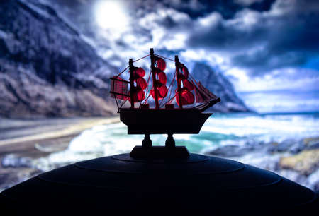 Beautiful boat toy over a blue balll with blurred night beach scene at background. Travel,...