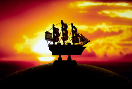 Beautiful boat toy over a blue balll with blurred red and orange sunset scene at background. Travel, adventure and journey conceptの写真素材