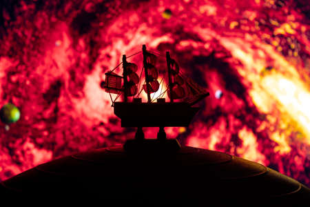 Beautiful boat toy over a blue balll with blurred red space vortex scene at background. Time travel, universe and space conceptの写真素材