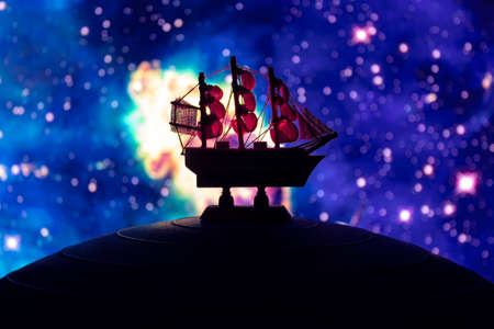 Beautiful boat toy over a blue ball with blurred multicolor nebula scenete at background. Travel, universe and space conceptの写真素材