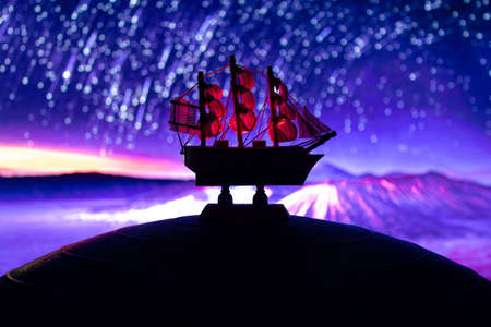 Beautiful boat toy over a blue balll with blurred violet stars, crescent mooon and a tree at...