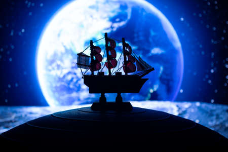 Beautiful boat toy over a blue balll with blurred blue planet and cosmos scene at background. Travel, universe and space conceptの写真素材