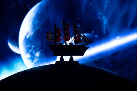 Beautiful boat toy over a blue balll with blurred blue planet and cosmos scene at background. Travel, universe and space conceptの写真素材