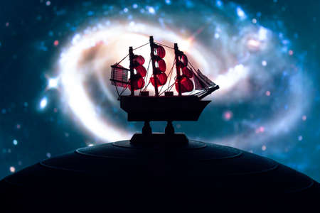 Beautiful boat toy over a blue balll with blurred multicolor spiral galaxy image at background. Travel, universe and space conceptの写真素材