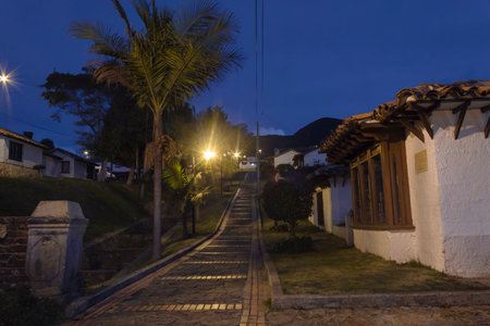 GUATAVITA, COLOMBIA - Colombian guatavita colonial town night scene of an empty brick pedestrian path near to a grass canal and a white house.のeditorial素材