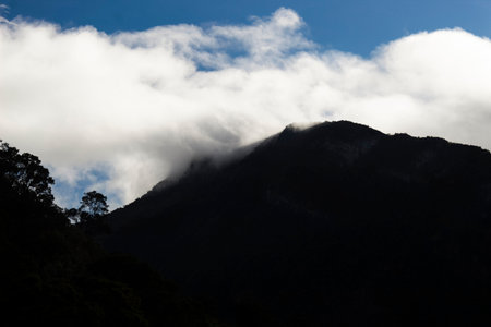 white clouds over a big andean forest mountain silhouette with blue sky at background