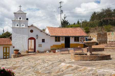 A reconstruction of an old colombian colonial town downtown square with principal church, small houses with ceramic roof and stone center font.のeditorial素材