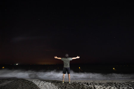 Young man with open arms watching the starry night at Santa Marta city beachの写真素材